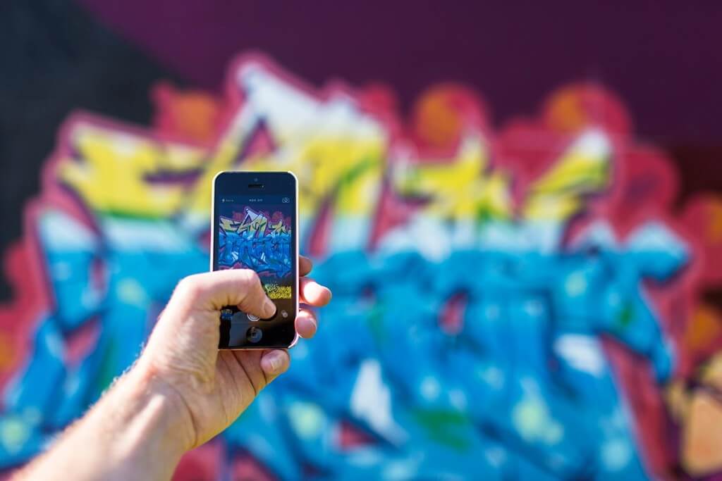 Hand photographing colorful graffiti with a smartphone.